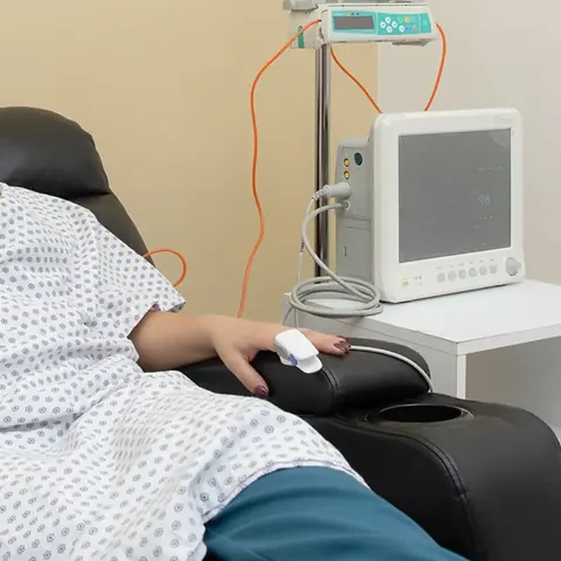 Paciente en sillón reclinable con oxímetro y monitor de signos vitales durante la infusión